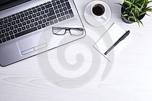 Top view of office work space, wooden desk table with laptop notebook,keyboard ,pen,eyeglasses,phone,notebook and cup of coffee.