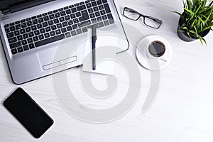 Top view of office work space, wooden desk table with laptop notebook,keyboard ,pen,eyeglasses,phone,notebook and cup of coffee.