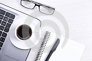 Top view of office work space, wooden desk table with laptop notebook,keyboard ,pen,eyeglasses,phone,notebook and cup of coffee.