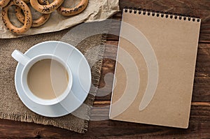 Top view office workplace: Ð¡ardboard notepad with bagels and coffee on wooden table