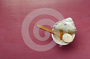 Top view ofopened yogurt cup and wooden spoon on it, pink background.Empty space
