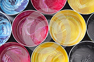 Top view of old CMYK paint cans on dark background. Colorful bac