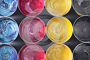 Top view of old CMYK paint cans on dark background. Colorful bac