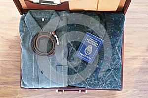 Top view of old suitcase with clothes and passport on wooden flo