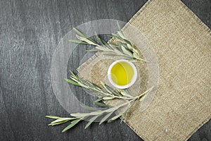 Top view of olive oil in a bowl, on wooden background. Olive oil with branches. Natural olive oil in white plate with branches aro