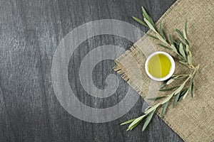 Top view of olive oil in a bowl, on wooden background. Olive oil with branches. Natural olive oil in white plate with branches aro