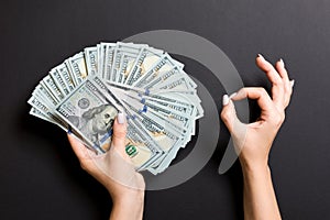 Top view of one hundred dollar bills in one hand and showing okay gesture with another hand on colorful background. Prosperity and