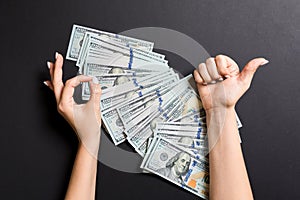 Top view of one hundred dollar bills in one hand and showing okay and thumb up gesture with another hand on colorful background.