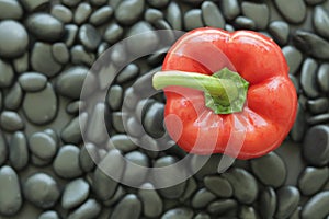Top view one red bell pepper on black stone that has smooth glossy skin and round edge.