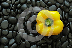 Top view one yellow bell pepper on black stone that has smooth glossy skin and round edge.