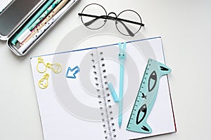 Top view of an open blank notebook with a blue hare-shaped pen, a ruler with a cat, glasses