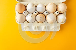 Top view of open egg box with ten brown and white eggs isolated on yellow background. Fresh organic chicken eggs.