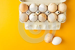 Top view of open egg box with ten farm eggs and two eggs near isolated on yellow background. Fresh organic chicken eggs.