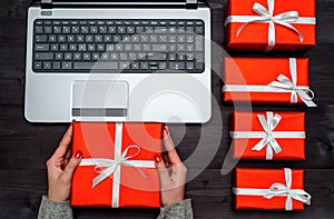 Top view of open laptop computer, red gift boxes on wooden table, copy space. Flat lay. Online shopping, sales. Woman holding.