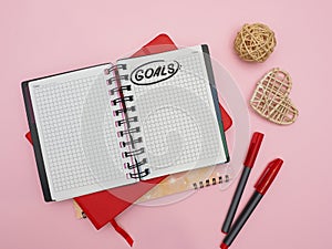 Top view of an open notebook with blank pages and goal inscription on pink table