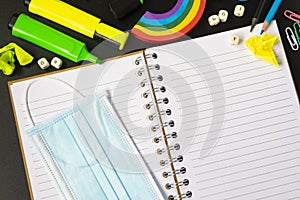 Top view of open notebook with face mask, colorful pencils, rainbow eraser, notebook, sticky notes. Flat lay.