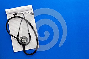 Top view of an open notebook with Medical stethoscope on a blue background.