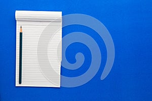 Top view of an open notebook with pencil on a blue background.