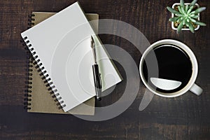 Top view of open school notebook with blank pages, Pen, Plant and Coffee cup on wooden table background. Business, office or educa