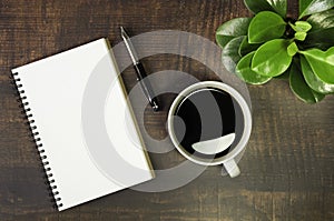 Top view of open school notebook with blank pages, Pen, Plant and Coffee cup on wooden table background. Business, office or educa