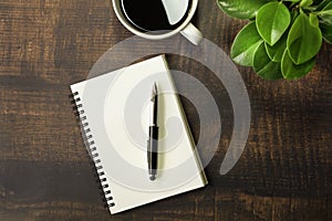 Top view of open school notebook with blank pages, Pen, Plant and Coffee cup on wooden table background. Business, office or educa