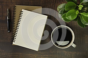 Top view of open school notebook with blank pages, Pen, Plant and Coffee cup on wooden table background. Business, office or educa