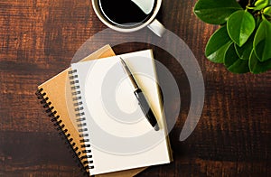 Top view of open school notebook with blank pages, Pen, Plant and Coffee cup on wooden table background. Business, office or educa