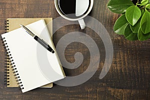 Top view of open school notebook with blank pages, Pen, Plant and Coffee cup on wooden table background. Business, office or educa