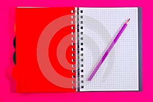 Top view of open spiral blank notebook with pencil on red desk background