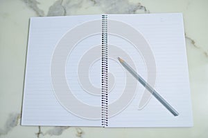 Top view of open spiral blank notebook with pencil on white desk background.