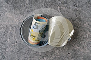 Top view of open tin can with a roll of Euro banknotes