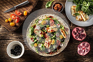 Top view of an open top vegetarian tortilla with salad, raddish, chery tomatoes, olives, pomegranate and grilled haloumi cheese photo