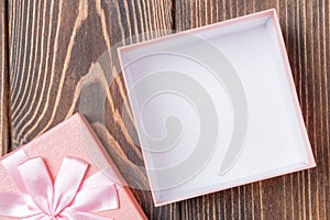 Top view of opened empty decorative pink gift box with bow on brown wooden table