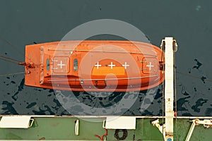 Top view on the orange colour life boat with reflective tape stickers secured with davits.