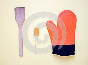 top view of orange cooking gloves, silicon potholders and kitchen tools on yellow background. Free copy space. Concept of home