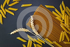 Top view Organic penne and whole wheat spaghetti pasta decorate by wheats on black slate stone plate