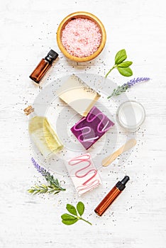 Top view of organic soaps and cosmetics arranged with lavender, herbs, chia seeds and essential oils. White rustic background