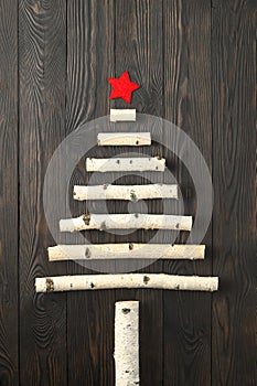 Top view of the original Christmas tree made of birch branches with a red star on a dark wooden background.