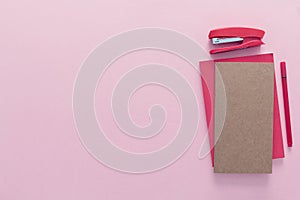 Top view over a school supplies as notebooks, pen and stepler from the right side of a pink background. Back to school concept. Of