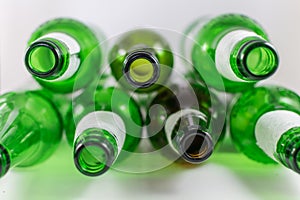 Top view of a pack of empty beer and wine green and brown glass bottles, with ripped labels on a white background. Reuse