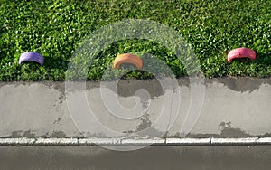 Top View Of Painted Colorful Old Tires As A Fence On The Green Grass Lawn Along The Asphalt Sidewalk With Stone Curb Near The Road