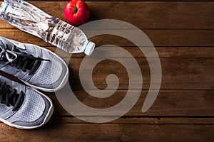 Top view of pair sports shoes, bottle water and red apple on wood table, Gray sneakers and accessories equipment in fitness GYM