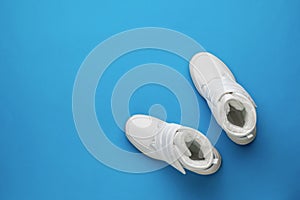 Top view of a pair of white women`s sports shoes on a blue background. Flat lay. Place for text