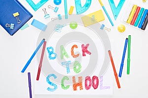 Top view of paper with back to school lettering near colorful felt-tip pens and stationery isolated on white.