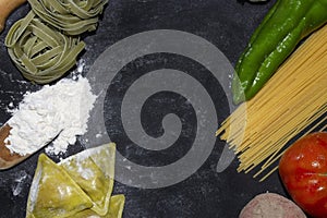 Top view of pasta background with spaghetti , ravioli,green pepper,onion and potato on floury dark background.Healthy homemade