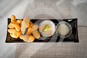 Top view of Patonggo or deep-fried dough sticks on black dish with pandan and sweet condense milk dipping on table