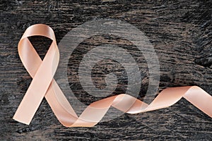Top view of peach ribbon on dark wood background. Uterine and endometrial cancer awareness concept.