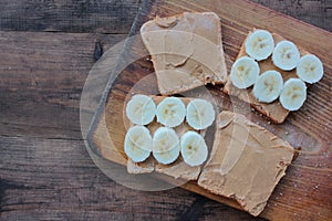 Top view of Peanut butter banana toasts on wooden background. Slices of whole wheat bran bread with peanut paste on cutting board