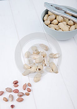 top view of peanuts in a bowl with nut cracker and shell on white background