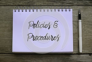 Top view of pen and notebook written with Policies and Procedures on wooden background